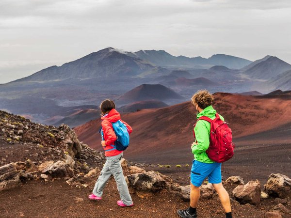Hawaii volcano hikers people walking hiking on mountains in Haleakala volcanic background landscape. Two young tourists couple on trek hike outdoors.