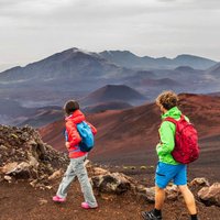 Hawaii volcano hikers people walking hiking on mountains in Haleakala volcanic background landscape. Two young tourists couple on trek hike outdoors.