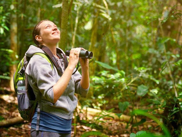 Hiker watching through binoculars wild birds in the jungle.