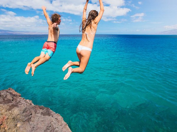Two adventurous millennial jump off a cliff into the sea while on vacation in Maui Hawaii