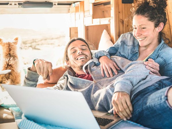A hipster couple browse freelance jobs on their laptop from the back of their van