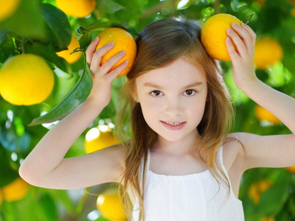 An adorable girl holds up two Florida oranges like mickey mouse ears on her head