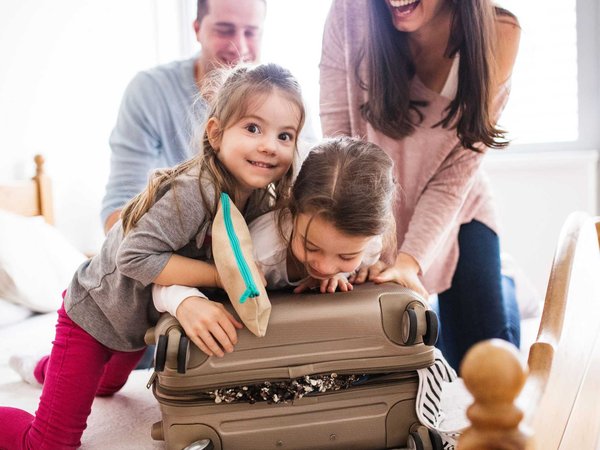 Mom and dad laugh while they pack a suitcase with two kids