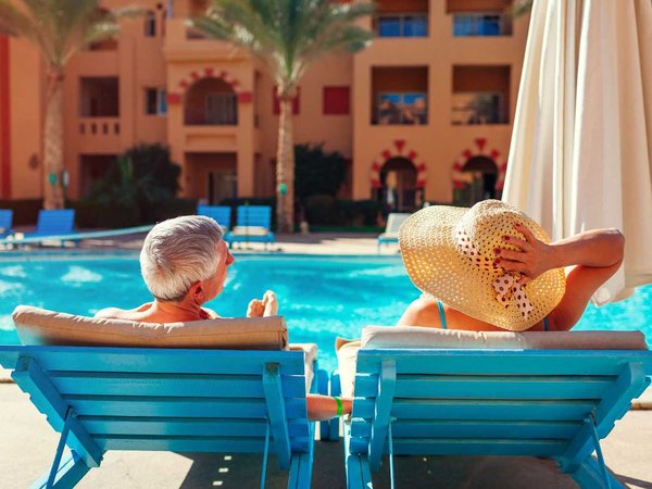 Senior couple relaxing by swimming pool lying on chaise-longues. People enjoying summer vacation.