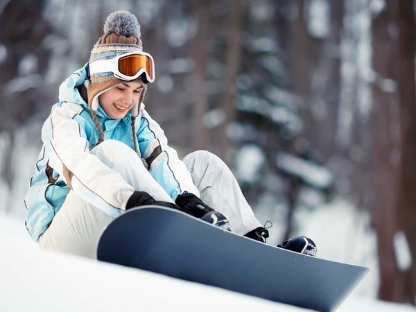 A woman tightens her boots to prepare for a snowboarding adventure