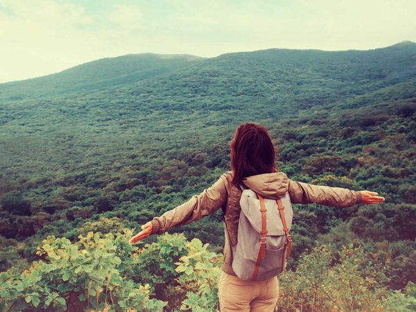 Woman spreads arms while standing on an overlook above a vast open forest
