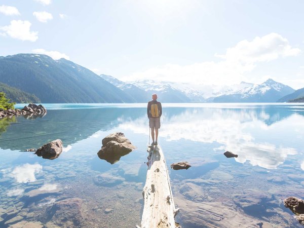 Man stands on the end of a log in a lake while looking out at a beautiful sunrise
