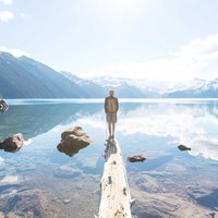 Man stands on the end of a log in a lake while looking out at a beautiful sunrise