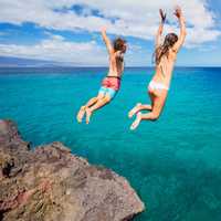 Two adventurous millennial jump off a cliff into the sea while on vacation in Maui Hawaii