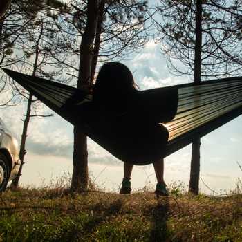 Girl in hammock in forrest near sea during sunrise chilling