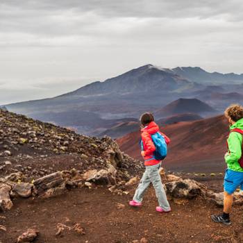 Hawaii volcano hikers people walking hiking on mountains in Haleakala volcanic background landscape. Two young tourists couple on trek hike outdoors.